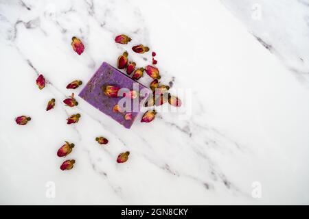Lavendel duftende Seifenstück umgeben von Rose Knospen auf Marmor Hintergrund Textur Stockfoto
