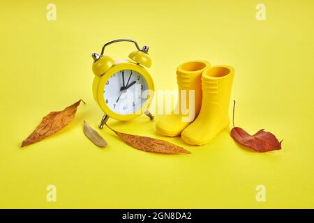 Fall Back Sommerzeit-Konzept mit gelber Uhr, Stiefeln und Herbstblättern auf gelbem Hintergrund Stockfoto