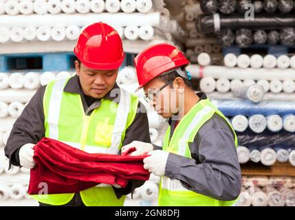 Zwei Arbeiter in der Textilfabrik überprüfen im Lager die Farbe des Rohstoffs rot Stockfoto