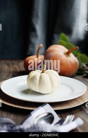 Festlich eingerichtet mit Teller, Serviette und Besteck an einem mit Thanksgiving-Tag dekorierten Tisch. Weiße und orangefarbene Kürbisse. Selektiver Fokus mit Unschärfen Stockfoto