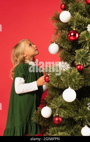 Mädchen in grünem Kleid Blick auf geschmückten weihnachtsbaum isoliert auf rot Stockfoto