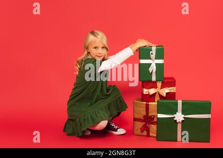 Mädchen in grünem Kleid lächelt an der Kamera in der Nähe Stapel von Geschenk-Boxen auf rot Stockfoto