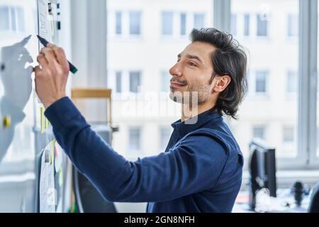 Geschäftsmann, der im Büro auf dem Whiteboard schreibt Stockfoto