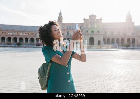Lächelnde weibliche Touristen, die per Smartphone auf der Plaza De Espana, Sevilla, Spanien fotografieren Stockfoto