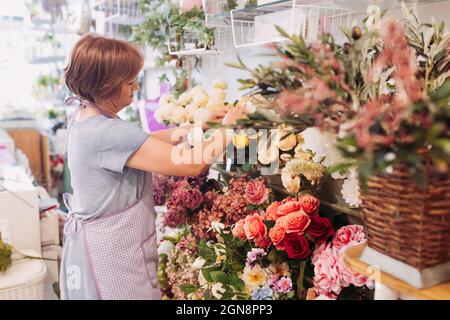 Reife weibliche Floristin, die Blumen arrangiert, während sie im Geschäft arbeitet Stockfoto