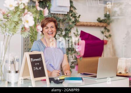 Ältere weibliche Blumengeschäft Besitzer lachen, während an der Kasse stehen Stockfoto