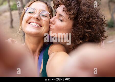 Lächelnde Frau beim Selfie mit einem Freund, der sich auf der Wange küsst Stockfoto