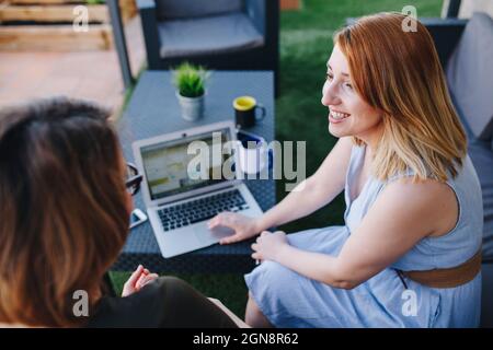 Eine professionelle Frau, die mit einer Kollegin diskutiert, während sie auf dem Dach mit einem Laptop sitzt Stockfoto
