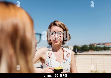 Geschäftsfrau mit Kaffeetasse, die an sonnigen Tagen mit Kollegen spricht Stockfoto