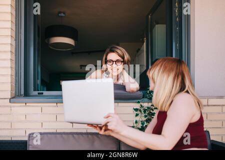 Geschäftsfrau, die einem Kollegen, der sich am Fenster stützt, einen Laptop vorführt Stockfoto