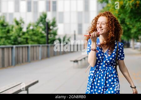 Glückliche junge Frau, die beim Gehen Voicemail schickte Stockfoto