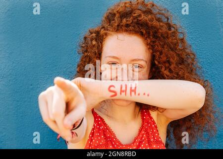 Lockige Frau, die mit Text auf dem Handgelenk vor der Wand zeigt Stockfoto