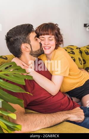 Bärtiger Mann, der zu Hause Freundin auf dem Sofa küsst Stockfoto