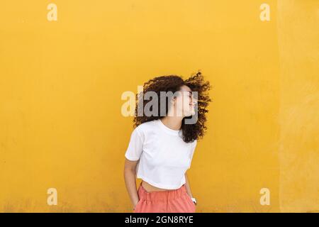Frau wirft Haare vor die gelbe Wand Stockfoto