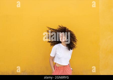 Sorglose Frau, die Haare vor die gelbe Wand wirft Stockfoto