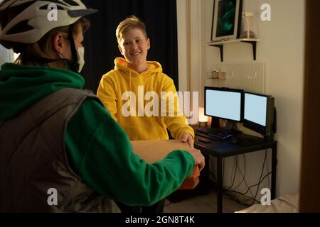 Lächelnder Junge, der während des COVID-19 Pizza von einer weiblichen Entbindung zu Hause nahm Stockfoto