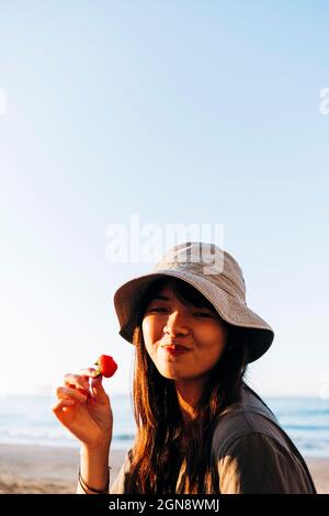 Schöne junge Frau, die am Strand Erdbeere isst