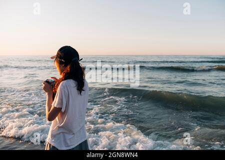 Junge Frau mit Kamera und Blick auf das Meer während des Urlaubs Stockfoto