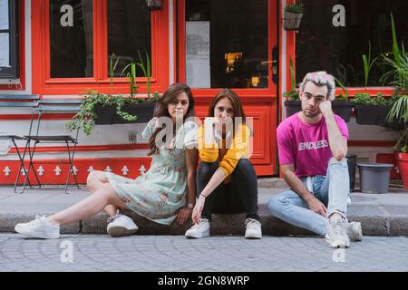 Schwuler Mann und weibliche Freunde sitzen zusammen auf dem Fußweg Stockfoto