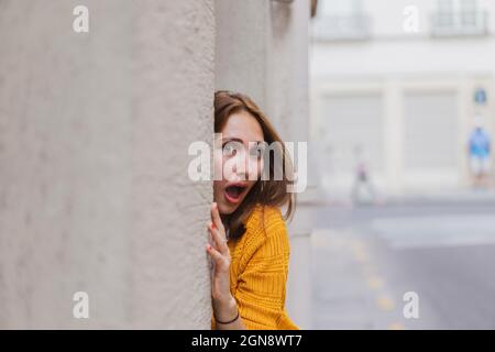 Überraschte Frau mit braunen Haaren, die von der Wand gucken Stockfoto