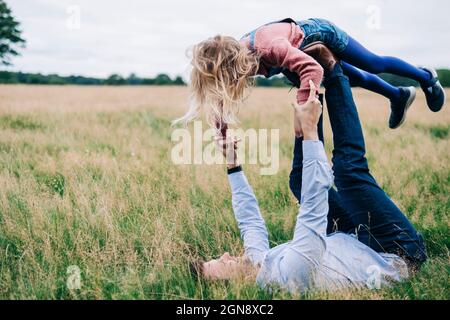 Verspielter Mann, der seine Tochter auf der Wiese aufholt Stockfoto