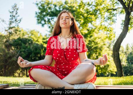 Frau, die Yoga praktiziert, während sie im Park mit gekreuzten Beinen sitzt Stockfoto