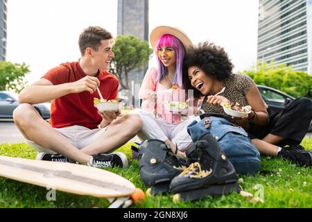 Fröhliche junge multiethnische Freunde essen Salat im Park Stockfoto