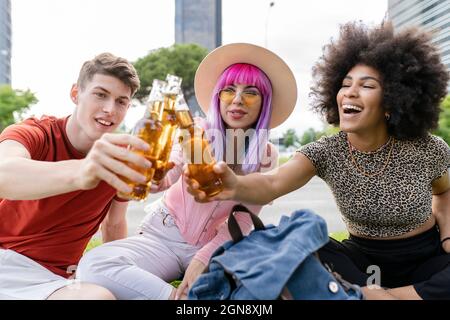 Multiethnische männliche und weibliche Freunde feiern während sie im Park sitzen Stockfoto