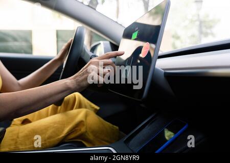 Frau, die ein digitales Tablet benutzt, während sie ein Elektroauto fährt Stockfoto