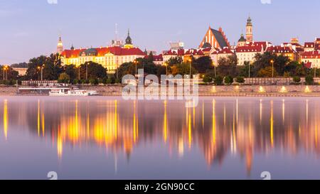 Beleuchtete Warschauer Altstadt-Panorama mit dem Königsschloss, der Kathedrale und mittelalterlichen Gebäuden, während des Sonnenaufgangs mit Reflexionen in der ruhigen Weichsel. Stockfoto