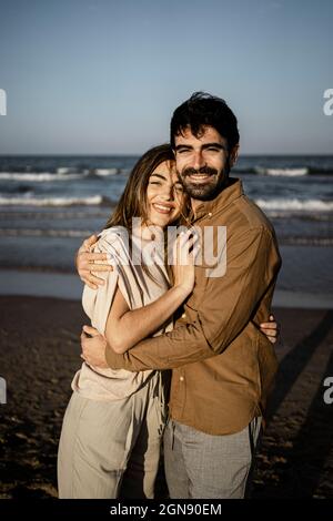 Lächelndes junges Paar umarmt sich am Strand Stockfoto