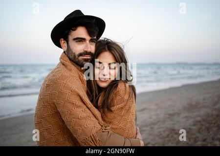 Junges Paar, das sich während des Sonnenuntergangs am Strand umarmt Stockfoto
