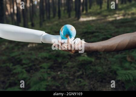 Mensch und Roboter halten Erdkugel im Wald zusammen Stockfoto