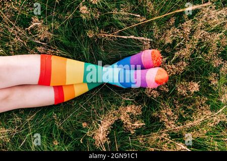 Frau trägt Regenbogensocken mit gekreuzten Beinen am Knöchel auf Gras Stockfoto