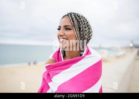 Junge Frau in Handtuch gewickelt, die am Strand steht Stockfoto