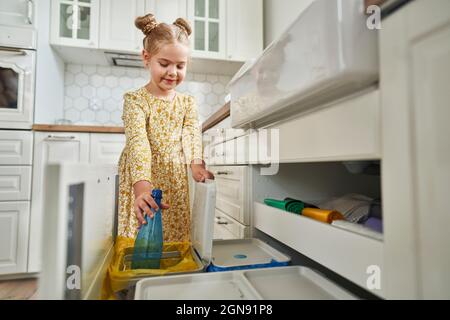 Mädchen mit Haarbrötchen, die Plastikflasche in den Abfalleimer werfen Stockfoto