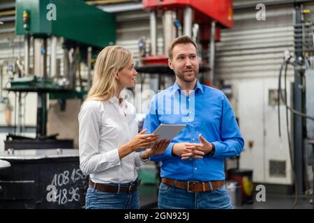 Männliche und weibliche Mitarbeiter mit digitalen Tablets diskutieren in der Industrie Stockfoto