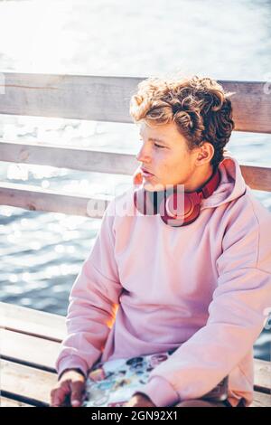 Junger Mann, der an sonnigen Tagen auf der Bank sitzt Stockfoto