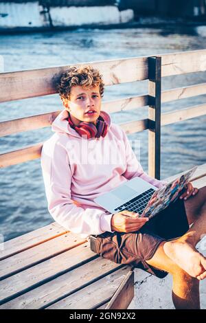 Hübscher Mann, der mit einem Laptop auf der Bank sitzt Stockfoto