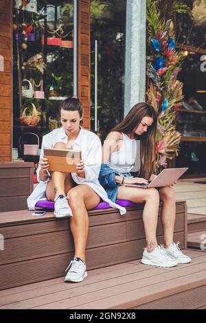 Weibliche Freunde, die auf der Bank ein digitales Tablet und einen Laptop verwenden Stockfoto