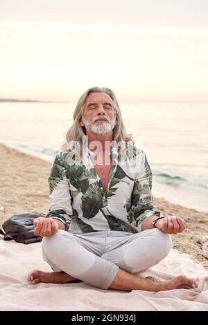 Mann mit grauen Haaren meditiert am Strand Stockfoto