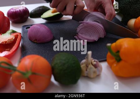 Koch schneidet rote Zwiebeln an Bord unter Gemüse aus der Nähe Stockfoto