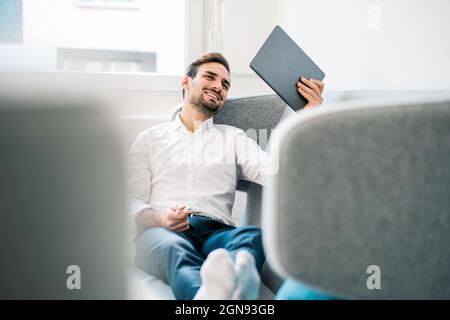 Glücklich entspannt männlichen professionellen Lesung digitale Tablette, während auf dem Sofa im Büro sitzen Stockfoto