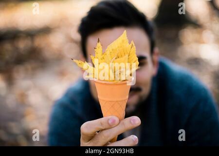 Junger Mann hält Eiskegel mit Blättern im Park Stockfoto