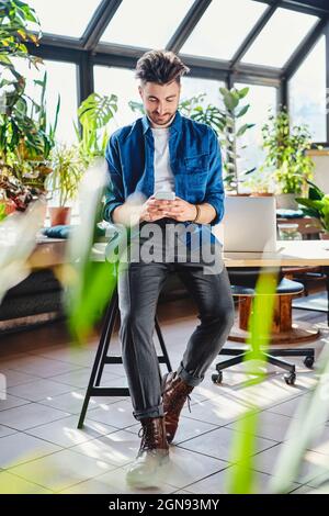 Junger Geschäftsmann, der im Büro über ein Smartphone im Internet surft Stockfoto