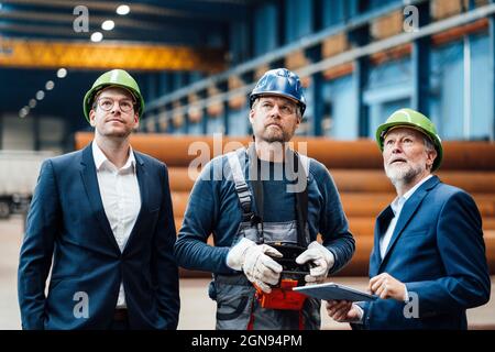 Männlicher Lagerarbeiter, der den Haken hält, während er in der Fabrik neben Kollegen steht Stockfoto