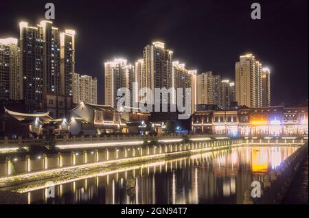 Beleuchtete Stadtlandschaft mit modernen Wolkenkratzern und traditionellen Häusern rund um den Teich Stockfoto