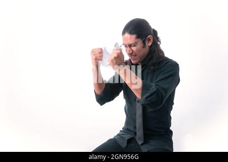 Mann auf weißem Hintergrund. Er zerreißt eine Seite, weil er sich über etwas ärgerte, das er gelesen hat. Er ist frustriert und hält seine Hände an seinen Kopf dres Stockfoto