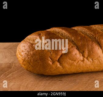 Teil eines Laib Brot, Nahaufnahme, auf einem Holzbrett auf schwarzem Hintergrund Stockfoto