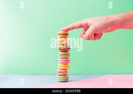 Hand eines jungen Mannes, der den Stapel pastellfarbener Makronen-Kekse berührt Stockfoto